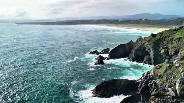 Nefes kesici manzara bulutlu bir gökyüzünün altında uzanan sakin bir turkuaz denizin yanında nefes kesici kayalık bir kıyı şeridi sergiliyor.