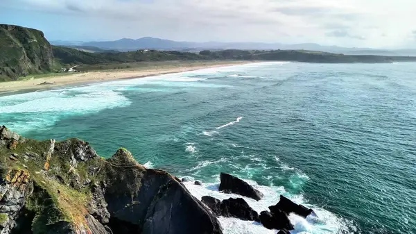 Sakin bir sahil manzarasında görkemli kayalıklara çarpan güçlü dalgaların nefes kesici ve çarpıcı manzaralarını keşfedin.
