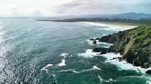 Muhteşem sahil şeridinin nefes kesici hava manzarasını deneyin, dalgalar görkemli kayalıklara çarpıyor.