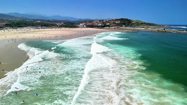 Güzel dalgalarla dolu canlı bir plaj sahnesi, neşeli güneş banyosu, ve her yerde büyüleyici manzaralar.