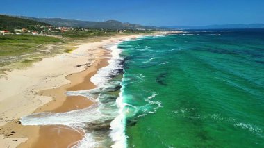 Çarpıcı bir deniz manzarası, canlı turkuaz dalgaların yanında sakin bir plajı güzelce sergiliyor.