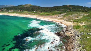 Sersemletici hava görüntüleri, turkuaz suların yer aldığı el değmemiş bir plajı ve etrafındaki sakin manzaraları gösteriyor.
