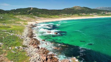 Havadan çekilen görüntüler turkuvaz suları, kayalık kıyıları ve yemyeşil alanları çevreleyen çarpıcı bir sahili yakalar.