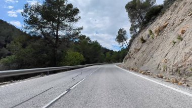 Kıvrımlı, kıvrımlı bir dağ yolunun nefes kesici manzarası, bereketli ağaçlar ve kayalık araziler tarafından güzel çerçevelenmiş.