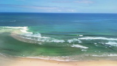 Sakin sahil dalgalarının ve berrak, güneşli bir gökyüzünün altındaki canlı mavi suların nefes kesici manzarasını hissedin.