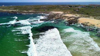 Canlı bir sahil sahnesinin nefes kesen görüntüsü dalgalarla sarmalanmış kayalık kıyıları sergiliyor.