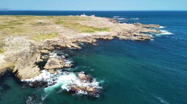 Çarpıcı hava manzaraları, parlak mavi gökyüzünün altında kristal berrak okyanus sularıyla buluşan dramatik kayalık bir kıyı şeridini vurguluyor.