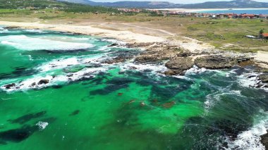 Sersemletici hava görüntüleri, güçlü dalgaları ve kayalık kıyıları olan yeşil ve mavi bir kıyı şeridini gösteriyor..