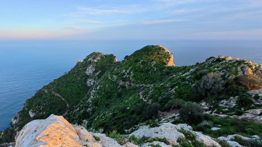 Serin denize bakan kayalık bir tepeden çarpıcı bir manzara, yemyeşil, canlı bitki örtüsüyle çevrili.