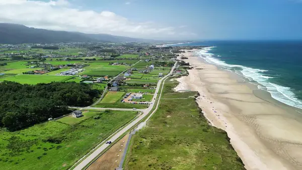 Güzel kumlu bir kumsalın yanında canlı yeşil tarlalar sergilenen kıyı bölgesinin nefes kesici hava manzarasının tadını çıkarın.