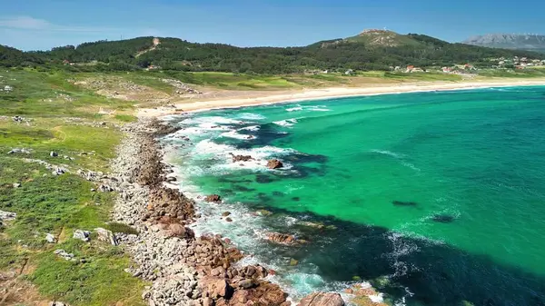 Havadan çekilen görüntüler turkuvaz suları, kayalık kıyıları ve yemyeşil alanları çevreleyen çarpıcı bir sahili yakalar.