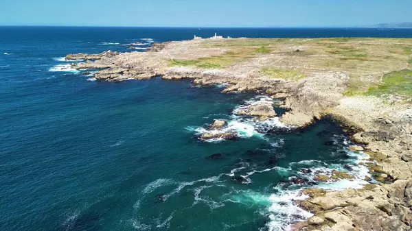Nefes kesici bir hava manzarası, engebeli kayalık kıyı şeritleri, berrak mavi sular ve uzak bir deniz feneri deneyin.