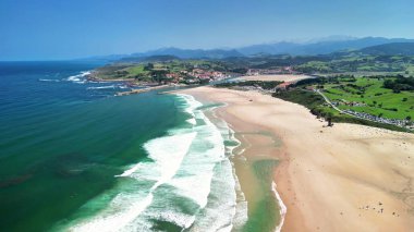 Yumuşak dalgaları ve çevresini saran yemyeşil tepeleri olan bir kumsalın nefes kesen görüntülerini tecrübe edin.