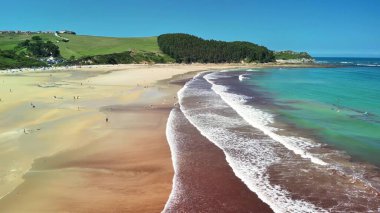Muhteşem bir sahil manzarası hayal edin. Altın kumlar üzerinde yumuşak dalgalar ve arka planda yemyeşil tepeler.