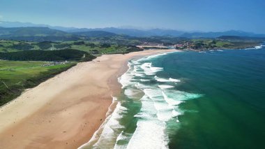 Nefes kesici sahil manzarası, parlak mavi gökyüzünün altında sersemletici altın kumlar ve berrak dalgalar sergiliyor.