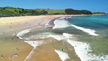 Güneşli bir günde dalgaların çarptığı, güneşlendiği ve yemyeşil tepelerin yeşerdiği çarpıcı bir sahil sahnesi.