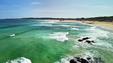Nefes kesici bir hava manzarası berrak turkuaz sular ve yumuşak dalgalarla süslenmiş sakin bir plajı gözler önüne seriyor.
