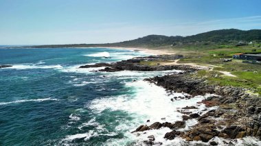 Açık gökyüzünün altındaki kayalık kıyılara çarpan dalgalarla sahilin nefes kesici güzelliğini yakalayın.