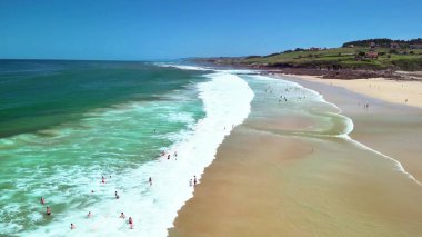 Çarpıcı bir plaj sahnesi. Canlı dalgalar çarpıyor ve güneşleniyor. Sıcak güneşin keyfini çıkarıyorlar.