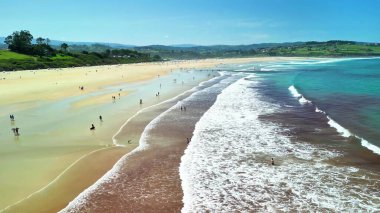 Güzel güneşli bir sahil, rahatlatıcı dalgaları olan, insanların dinlendiği ve nefes kesici kıyı manzaralarının tadını çıkardığı.