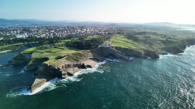 Canlı yeşillik ve kayalıklara çarpan dalgaların yer aldığı muhteşem bir kıyı manzarası..