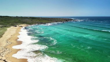 Bu sakin sahil sahnesinde turkuaz suların yumuşak kumlu kıyılarla harmanlanmasının güzelliğini hissedin..