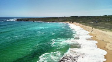 Nefes kesici bir hava manzarası, turkuaz suların ve parıldayan altın kumların yer aldığı huzurlu bir sahil sahnesini yakalıyor.