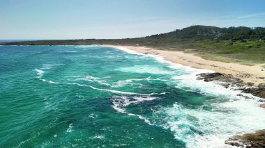 Bu hava manzarasında çarpıcı dalgalar, altın kum ve yemyeşil tepeler sergileniyor.