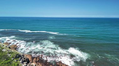 Okyanus dalgalarının nefes kesici ve büyüleyici görüntüsünü deneyimleyin. Açık mavi gökyüzünün altında sahil şeridine usulca yaklaşın.