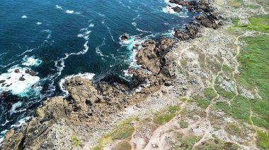 Okyanus kıyısındaki engebeli bir kıyı şeridine çarpan çarpıcı dalgaların nefes kesici hava görüntülerini tecrübe edin.