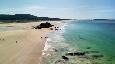 Kristal berraklığında turkuaz su ve manzaralı kayalık oluşumlarla sakin bir plajın nefes kesici ve çarpıcı bir görüntüsü.