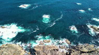 Çarpıcı hava manzarası dinamik okyanus dalgalarının aşağıdaki engebeli kıyı kayalarına çarptığını gösteriyor.