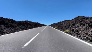 Açık mavi gökyüzünün altındaki engebeli, nefes kesici volkanik arazide uzun ve manzaralı bir yol uzanır.