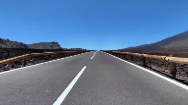 Güzel ve manzaralı bir yol, berrak mavi gökyüzünün altındaki engebeli lav arazisinde etkileyici bir şekilde uzanıyor.