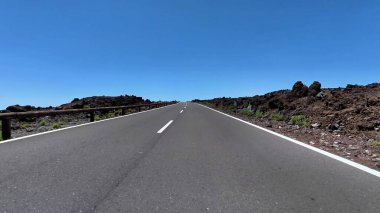 Açık mavi gökyüzünün altında eşsiz bir volkanik araziyi kesen uzun bir otoyolun büyüleyici görüntüsü..