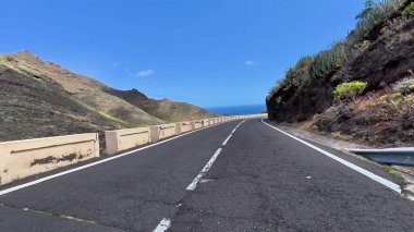 Arka planda okyanusla görkemli dağların arasında kıvrılan kıyı yolunun nefes kesici manzarasını deneyimleyin.