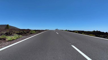 Çok güzel volkanik manzaralar ve açık mavi gökyüzü boyunca uzanan çarpıcı bir otoyolu olan pitoresk bir yol sahnesi.