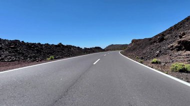 Resimli, dolambaçlı bir yol güzel, berrak bir mavi gökyüzünün altında çarpıcı volkanik arazide dolanıyor.