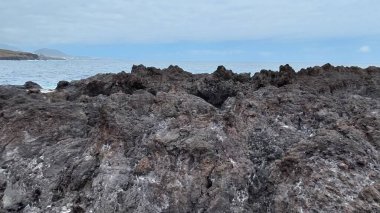 Kıyı şeridi boyunca uzanan engebeli kayaların çarpıcı manzarası bulutlu bir gökyüzünün altında güçlü dalgalar çarpıyor.