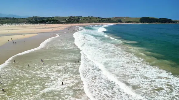 Çarpıcı bir hava manzarası dalgaların tadını çıkaran ve canlı bir sahilde güneşin tadını çıkaran kumsala gidenleri yakalıyor.
