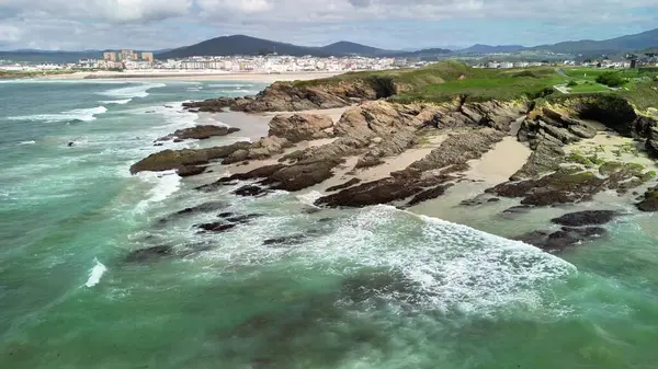 Engebeli bir kıyı şeridinin çarpıcı bir hava manzarası. Turkuaz suları akıyor ve yavaşça kıyıya çarpıyor.