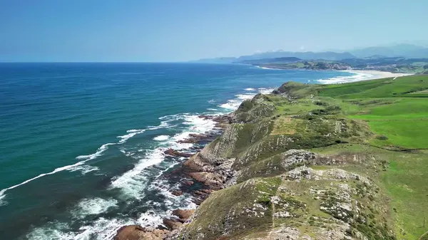 Berrak bir gökyüzünün altında canlı mavi okyanusla birleşen yemyeşil uçurumların çarpıcı hava manzarasını tecrübe edin.