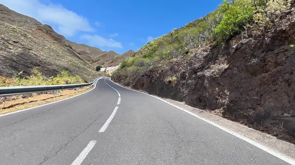 Görkemli dağlarla çevrili dolambaçlı bir yolun manzarası ve berrak mavi gökyüzünün altında yemyeşil bir yer.
