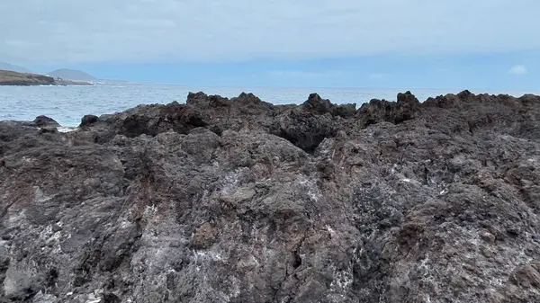 Kıyı şeridi boyunca uzanan engebeli kayaların çarpıcı manzarası bulutlu bir gökyüzünün altında güçlü dalgalar çarpıyor.