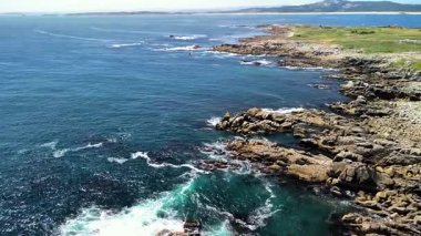 Nefis bir kıyı manzarası güzel bir şekilde sergilenen engebeli kayalar ve berrak bir gökyüzünün altındaki canlı turkuaz deniz.