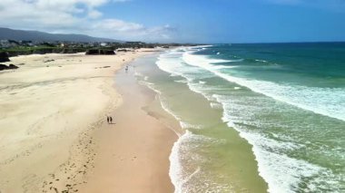 Güzel bir sahil, yumuşak altın kumu, yumuşak dalgaların kıyıya vurduğu ve insanların sahil boyunca dolaştığı
