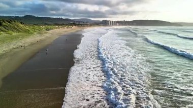 Muhteşem bir günbatımı manzarası sırasında kumlu bir sahilde usulca süzülen yumuşak dalgaların büyüleyici ve resimsel bir sahnesi.