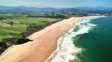 Canlı manzaralar ve kıyıya vuran berrak okyanus dalgalarıyla çevrili çarpıcı bir plajın havadan çekilmiş görüntüsü.