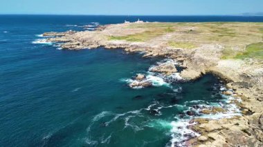 Nefes kesici bir hava manzarası, engebeli kayalık kıyı şeritleri, berrak mavi sular ve uzak bir deniz feneri deneyin.