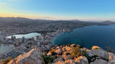 Güneş doğarken yüksek bir dağ zirvesinden güzel bir kıyı şehrinin nefes kesici panoramik manzarasını tecrübe edin.
